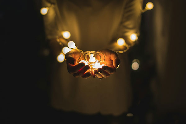Person holding a string of warm white fairy lights in their hands, set against a dark background.